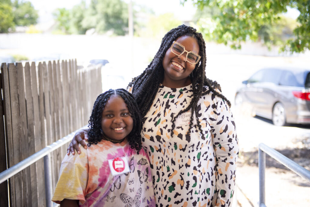 Tiffany Tigbo and daughter stand smiling in the sunshine