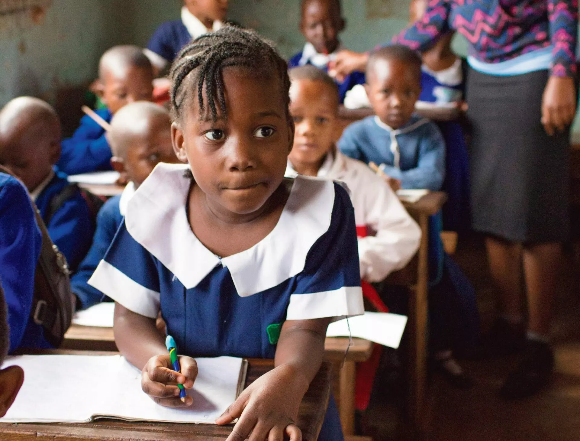 Young girl sits in a classroom at a desk writing with a pencil